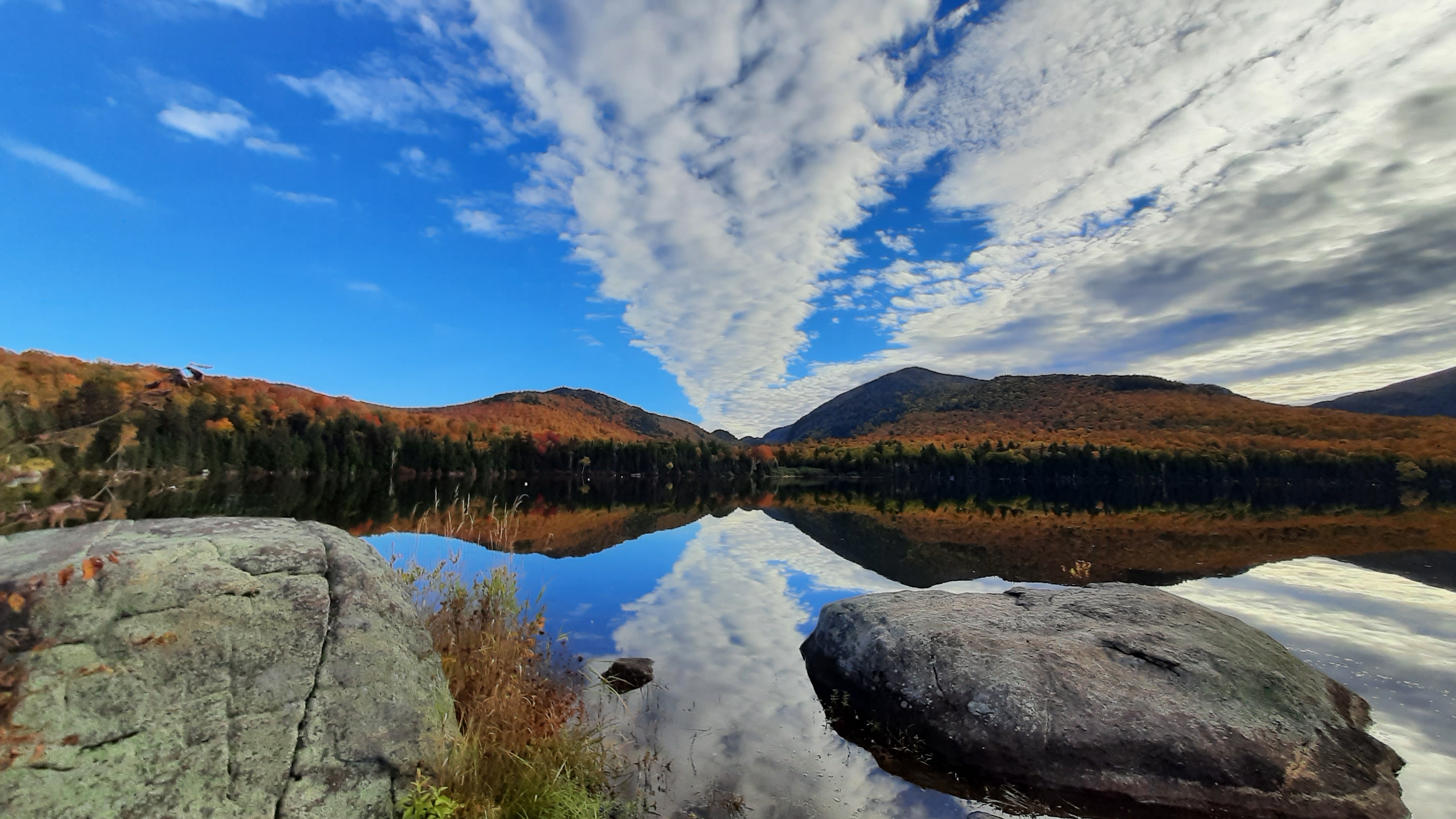 A peaceful lake in the Adirondacks during peak fall foliage with wispy clouds in a bright blue sky